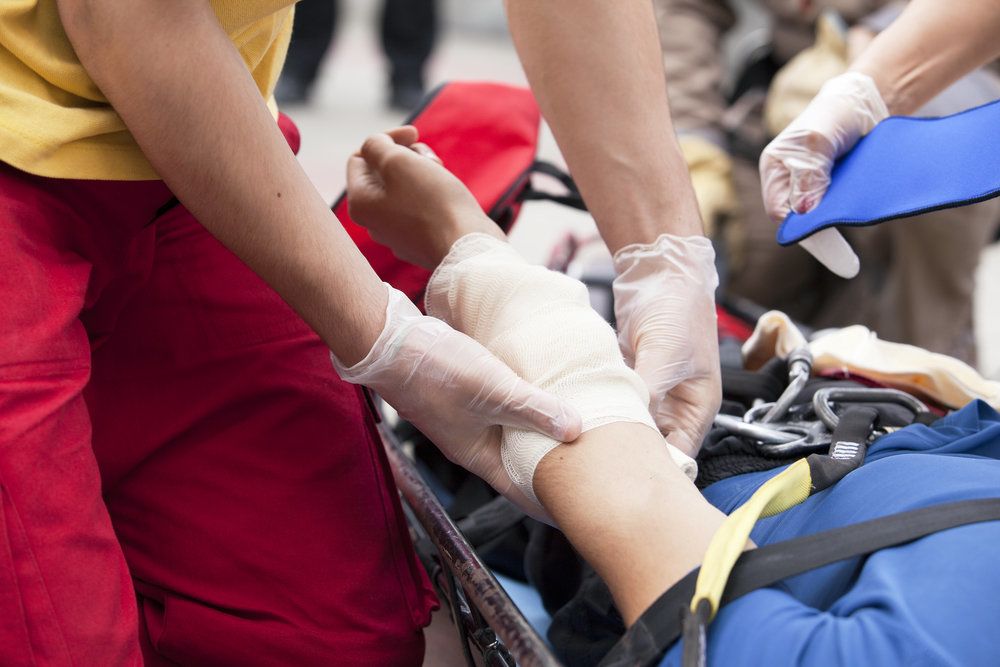 Close view of person on gurney with bandaged arm, tended to by a person wearing medical gloves